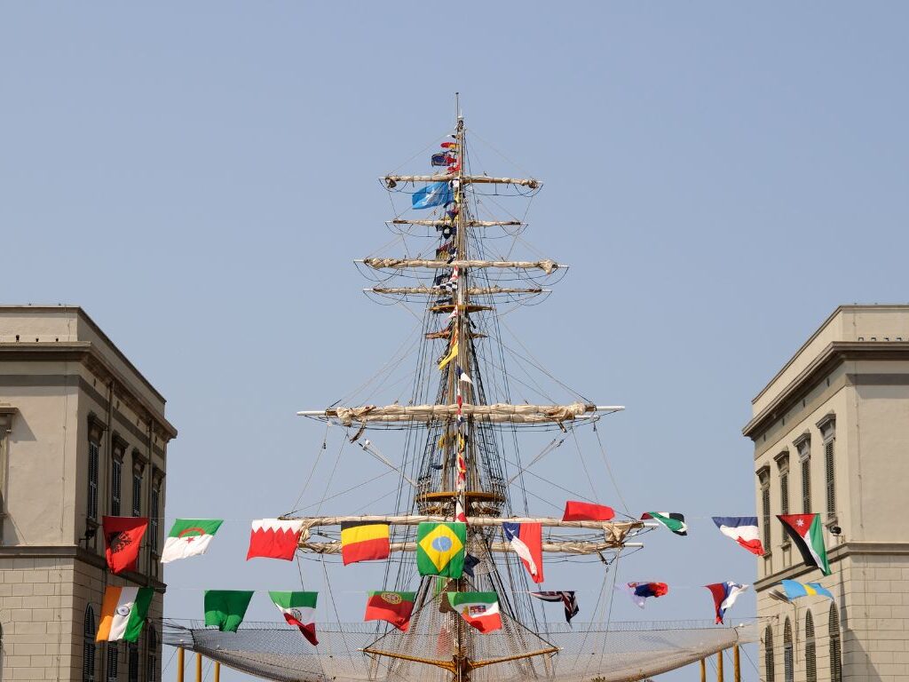 Ingresso dell’Accademia Navale di Livorno con torri gemelle e albero di nave decorato con bandiere, simbolo della Marina Militare Italiana.